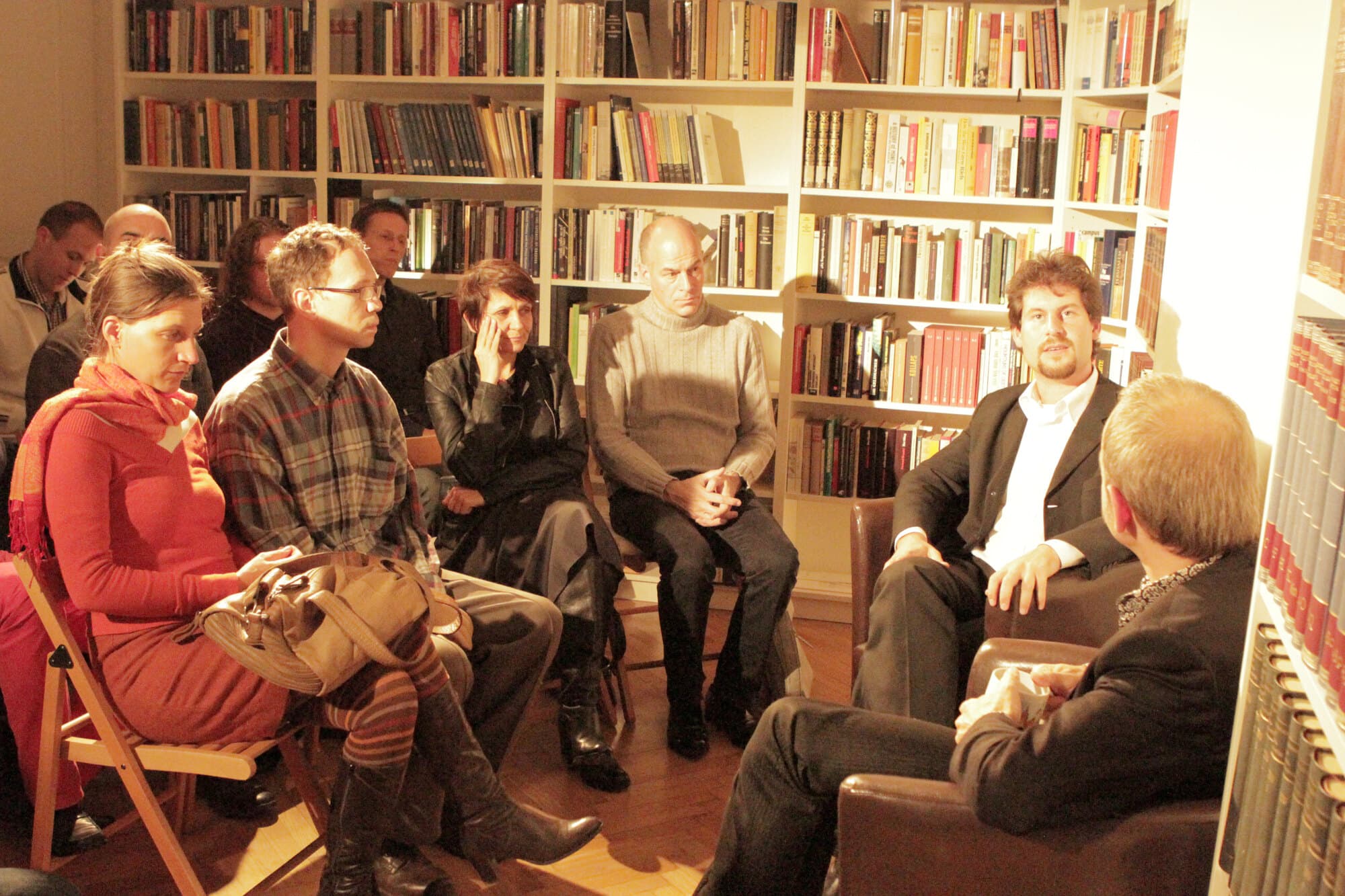 Teilnehmer sitzen in engem Kreis zwischen den Regalen der Wiener Bibliothek, während Rahim Taghizadegan spricht