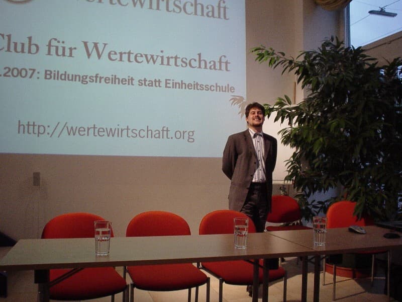 Rahim Taghizadegan vor einer Projektion des Clubs für Wertewirtschaft bei einer Veranstaltung in Wien